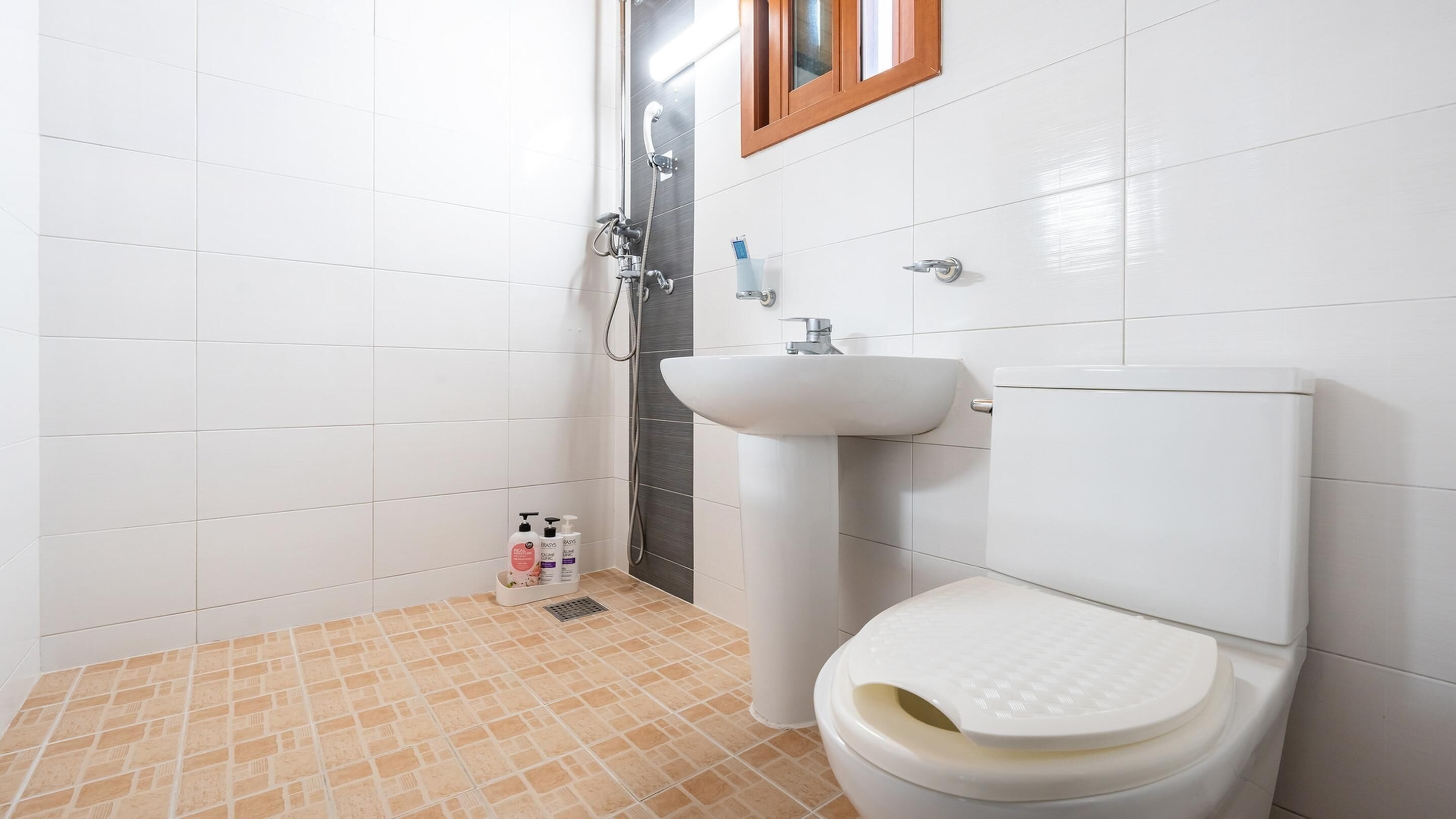 A bathroom with white tiles, a beige floor, a white sink, and a toilet.