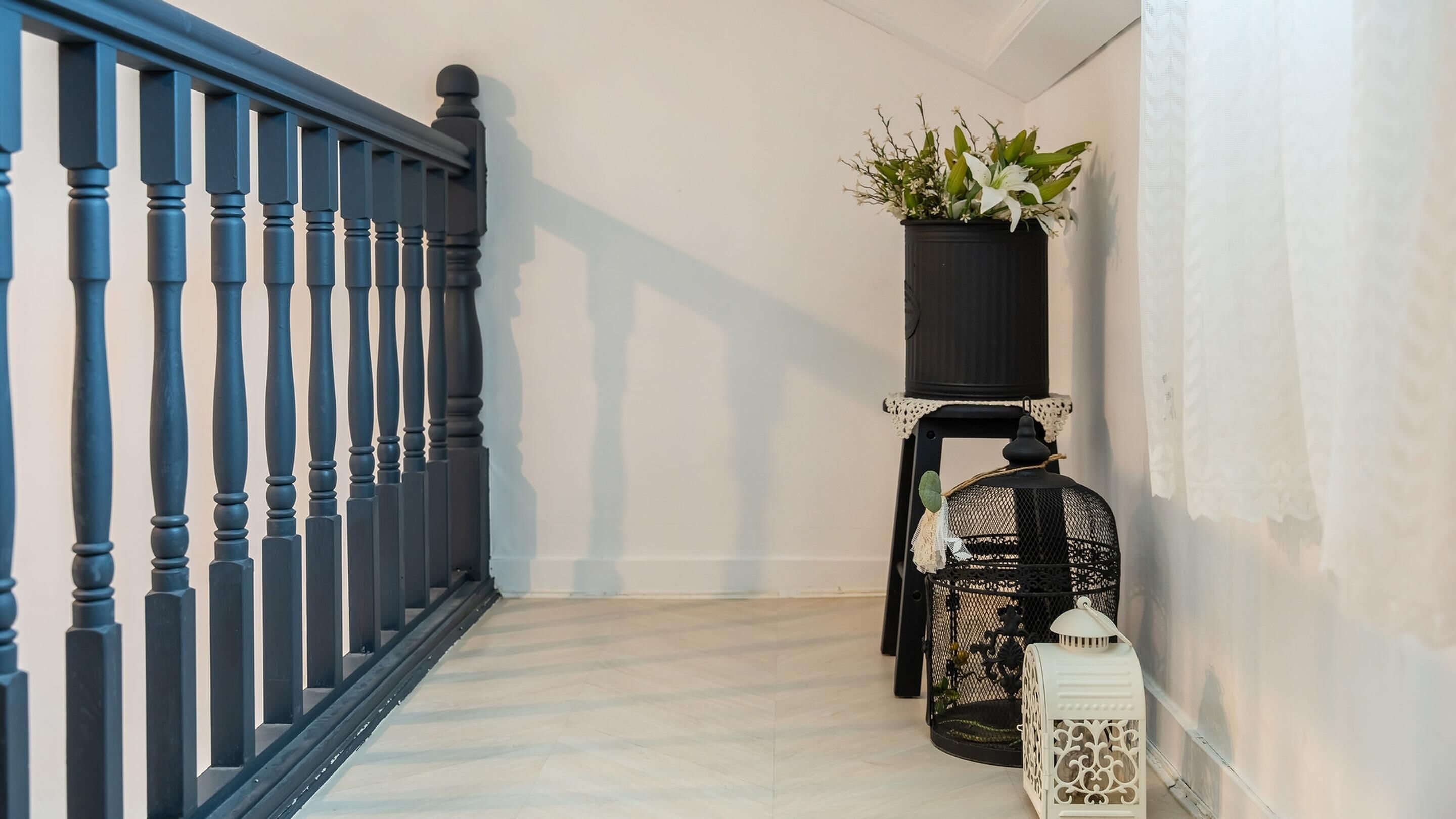A staircase with a black railing, a potted plant on a black stand, and a white lantern on the floor.