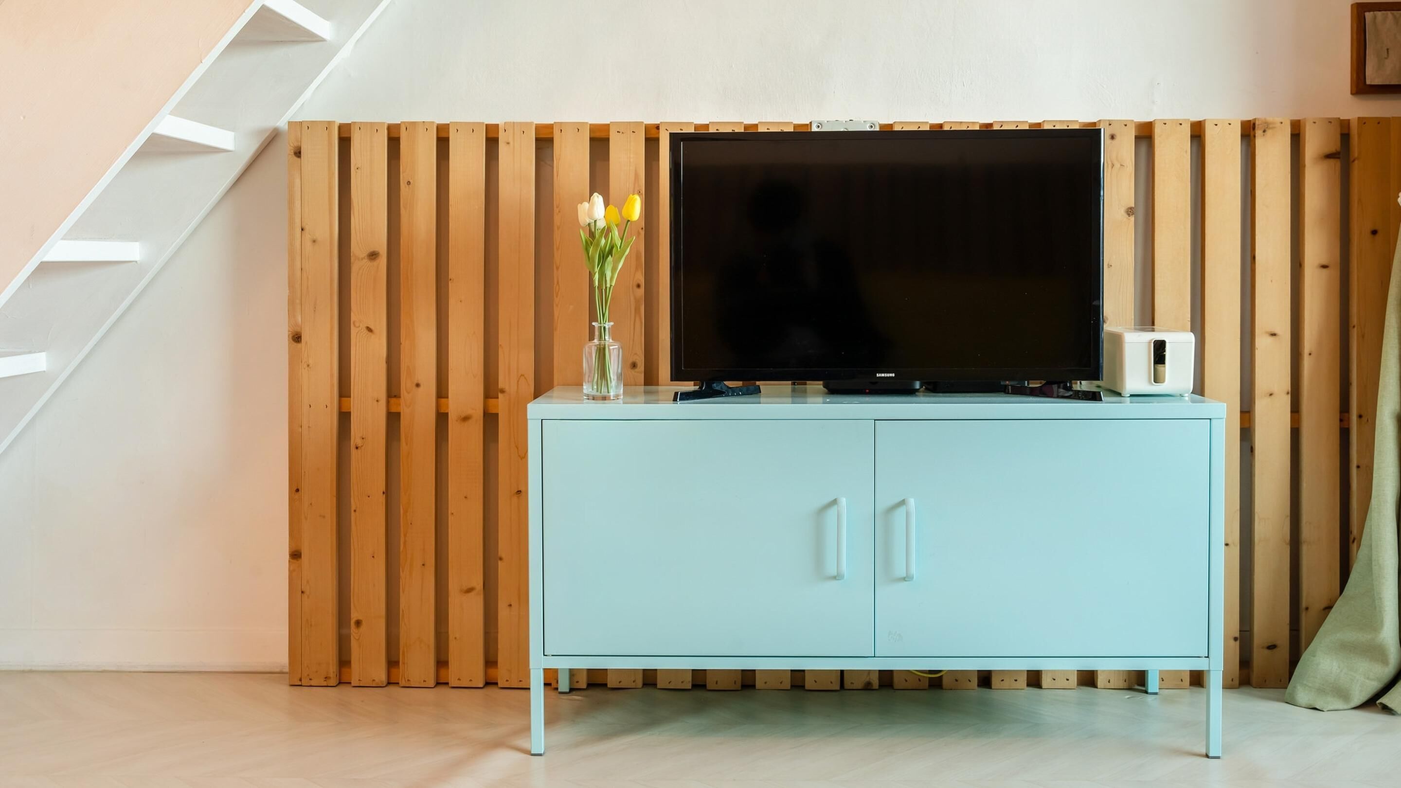 A room with a light blue cabinet, a flat-screen TV, and a wooden slat wall.