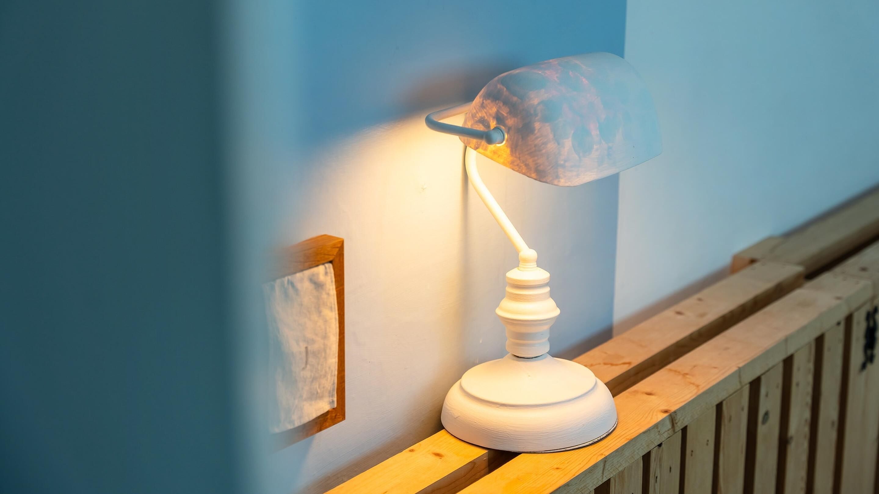 Een witte bureaulamp met een opvallende, geribbelde lampenkap op een houten leuning.
