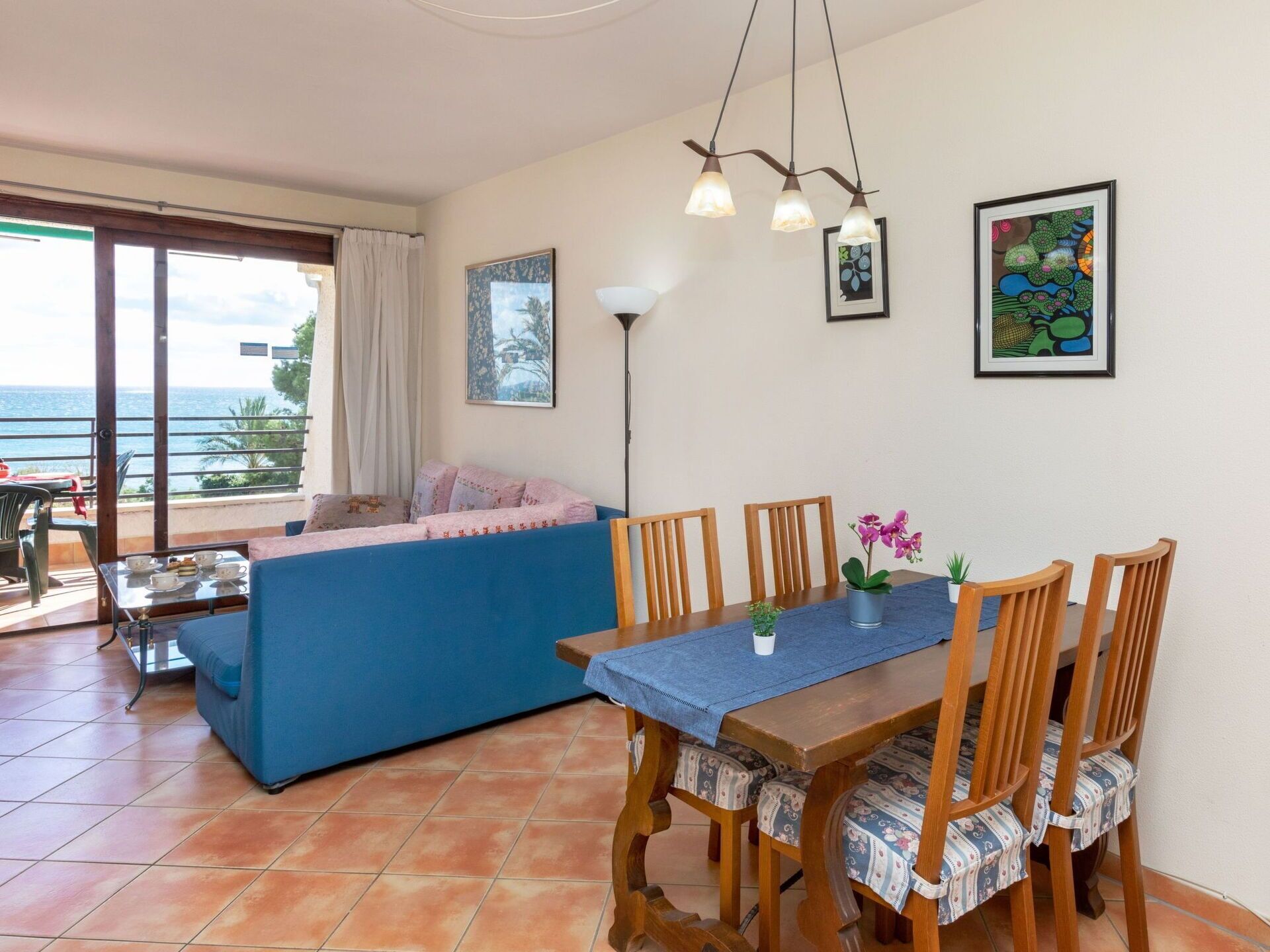 Zona pranzo con tavolo e sedie in legno, divano blu e vista mare attraverso ampie finestre.