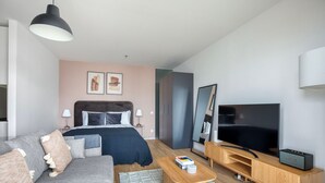 A modern hotel room with a bed, a sofa, a TV, and a wooden side table. - Favoriten Studio w Gym & Bike Storage, nr Metro by Blueground (Vienna)