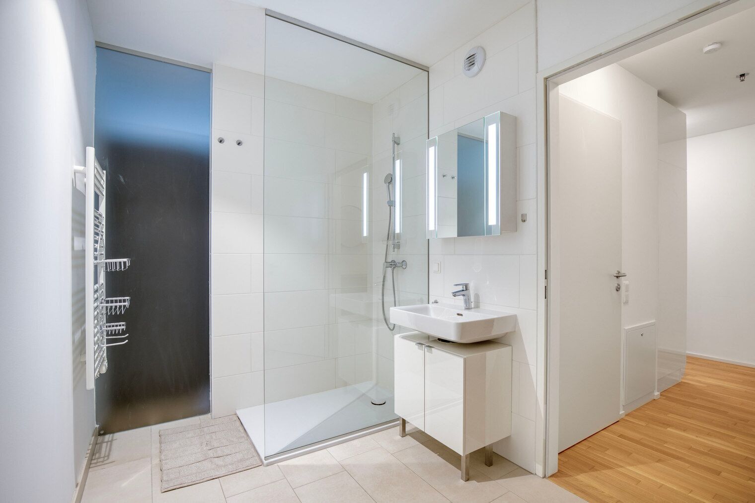 Une salle de bain moderne avec une douche à parois de verre, un lavabo avec un miroir et un plancher en bois.