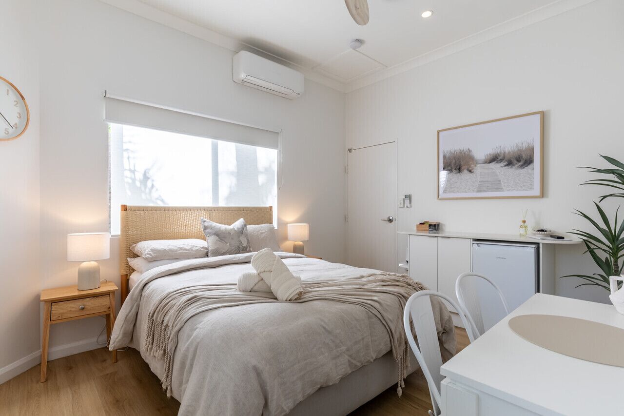 Et moderne soveværelse med seng, natbord, lampe og udsigt til stranden gennem vinduet.