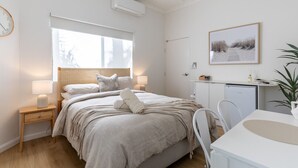 Une chambre à coucher moderne avec un lit, une table de chevet, une lampe et une vue sur la plage par la fenêtre.