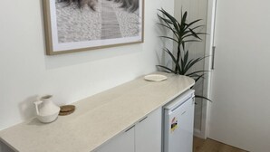 Un comptoir de cuisine avec un pichet blanc et un sous-verre, un petit réfrigérateur et une plante en pot.