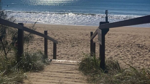 Un escalier en bois mène à une plage d’où l’on a une vue dégagée sur l’océan.