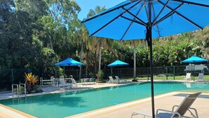Une piscine entourée d’une clôture et d’arbres, avec des chaises longues et des parasols.