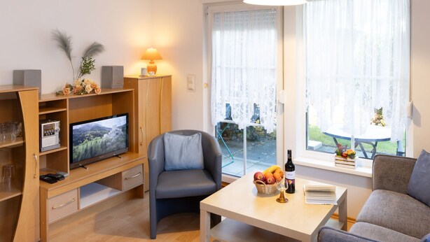 A modern living room with a flat-screen TV, a sofa, a dining table, and a large window with sheer curtains. - Apartment Kluge by Interhome (Zinnowitz)