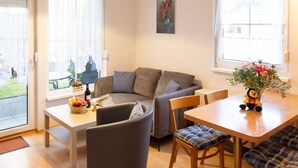 A cozy living room with a sofa, a dining table, and a window with a view of the outdoors. - Apartment Kluge by Interhome (Zinnowitz)