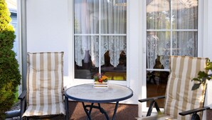 A patio with two striped chairs and a round table, a white exterior wall, and lace curtains on the windows. - Apartment Kluge by Interhome (Zinnowitz)