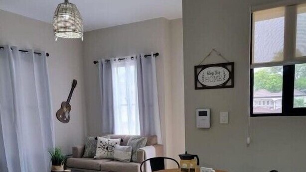 A cozy living room with a sofa, a coffee table, and a dining table with chairs. There is a guitar leaning against the wall and a hanging light fixture.