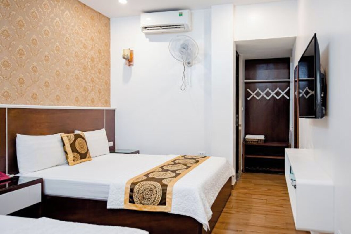 Een hotelkamer met een bed, nachtkastje, kledingkast en een aan de muur bevestigde televisie.