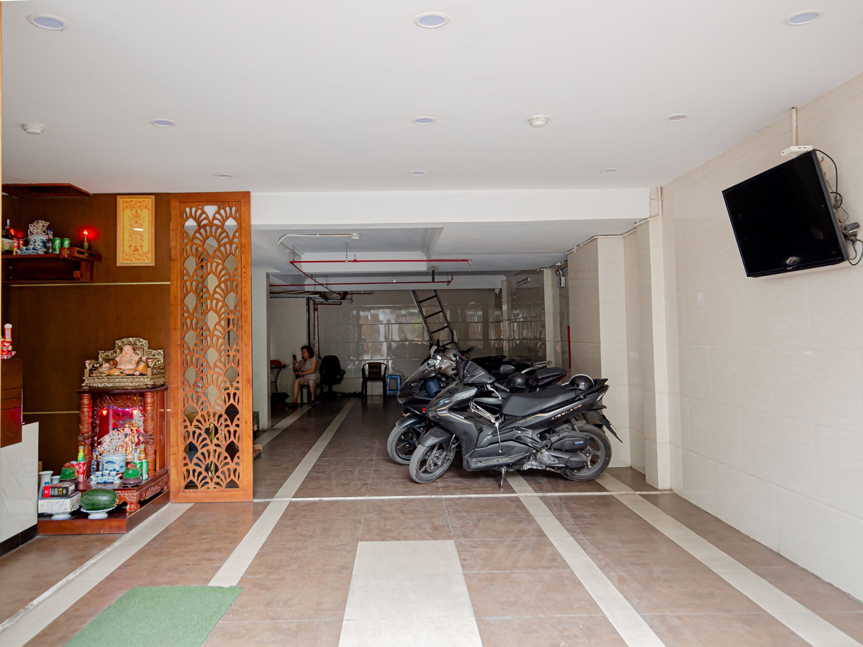 A hallway with a motorcycle parked on the right, a TV mounted on the wall, and a decorative wooden panel on the left.