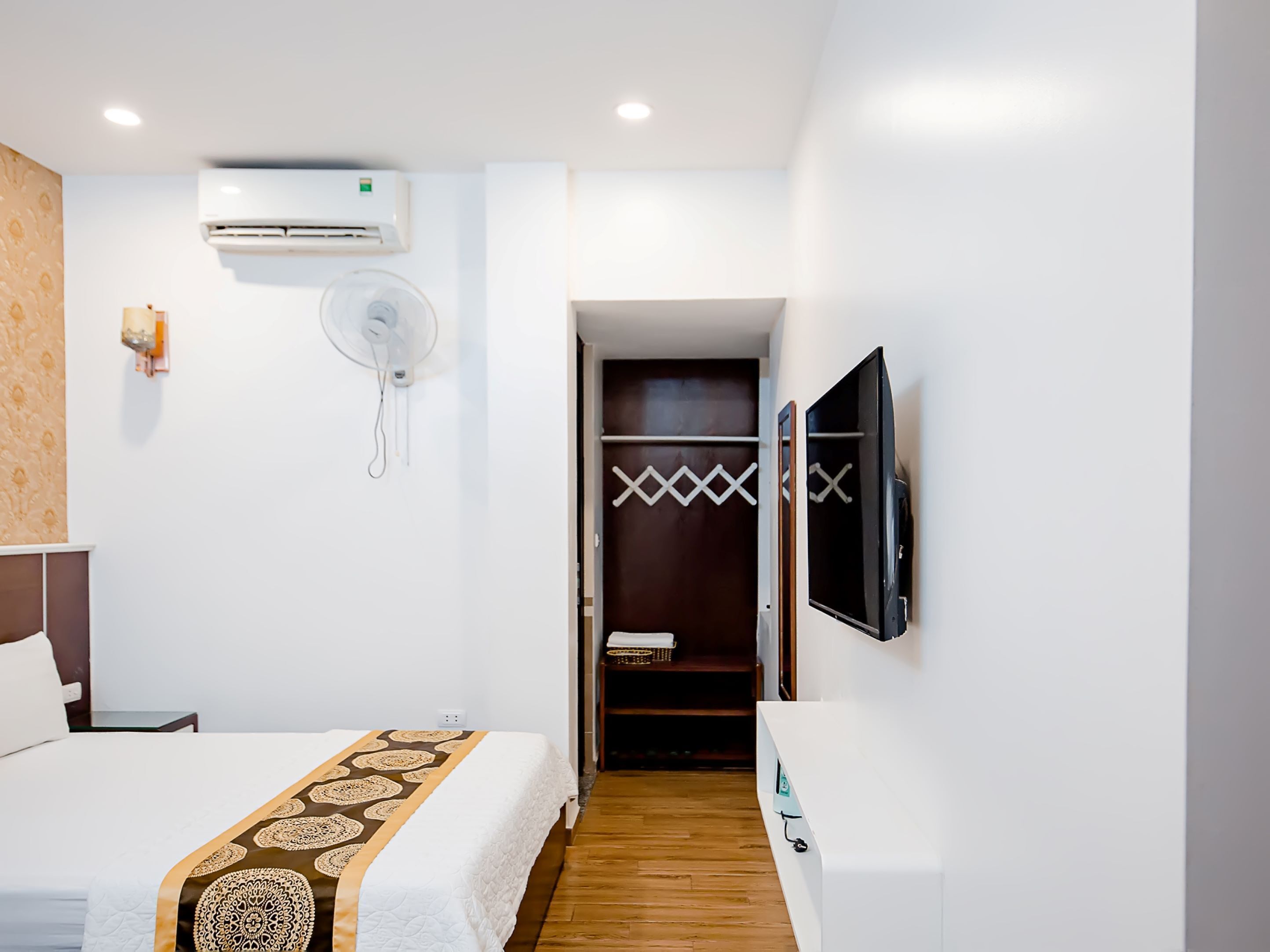 A hotel room with a bed, an air conditioning unit, a fan, a TV, and a wardrobe.