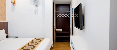 A hotel room with a bed, an air conditioning unit, a fan, a TV, and a wardrobe.