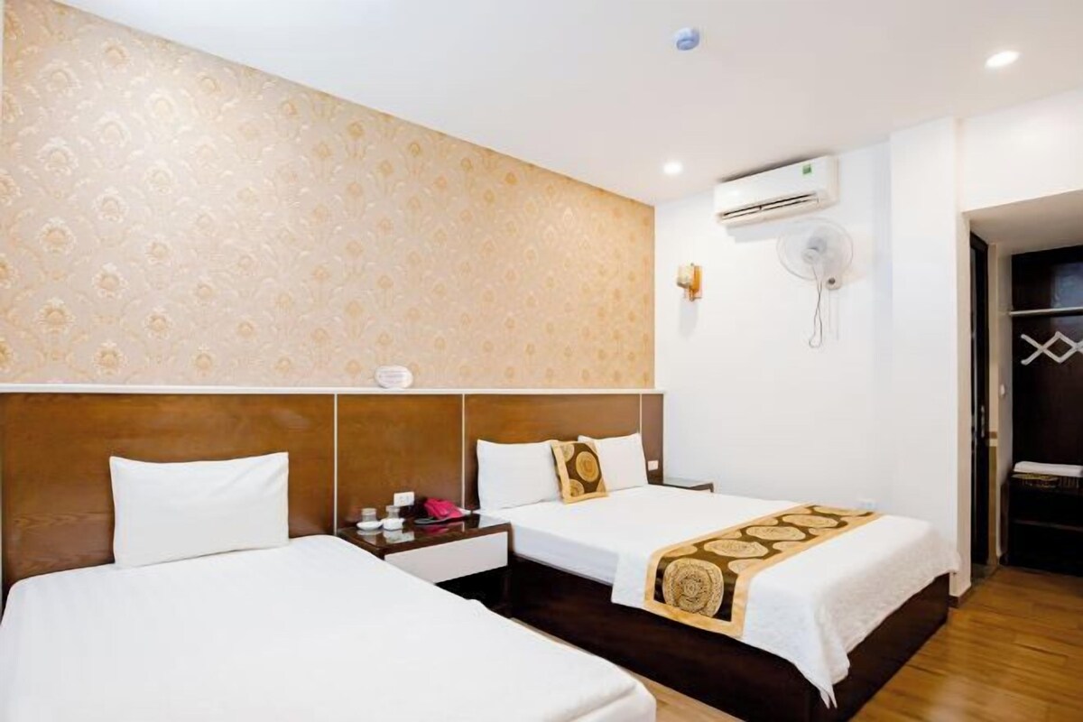 A hotel room with two beds, a wooden headboard, a patterned wall, an air conditioning unit, and a fan.