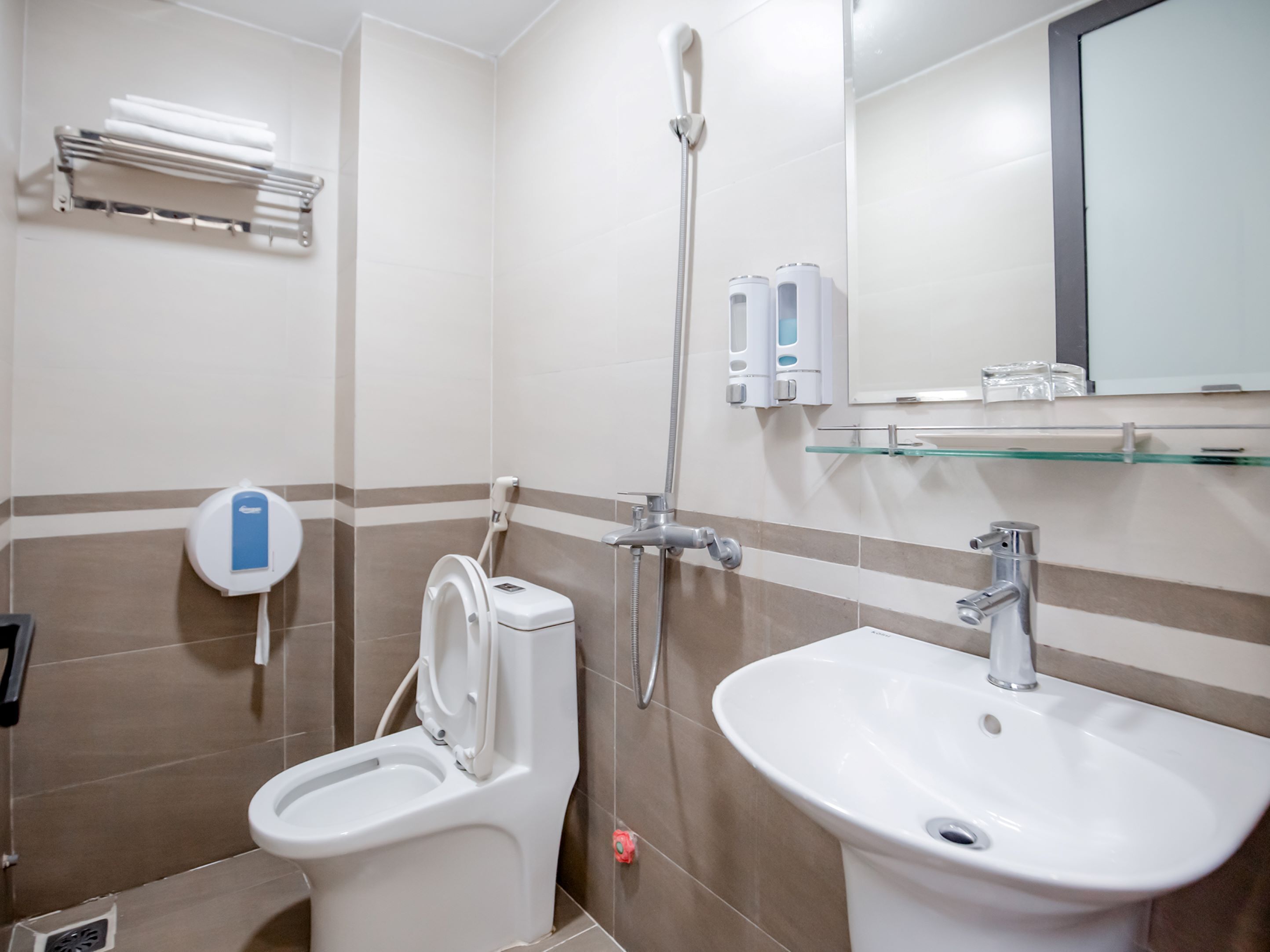 Een badkamer met toilet, bidet, wastafel en een glazen plank met toiletartikelen.