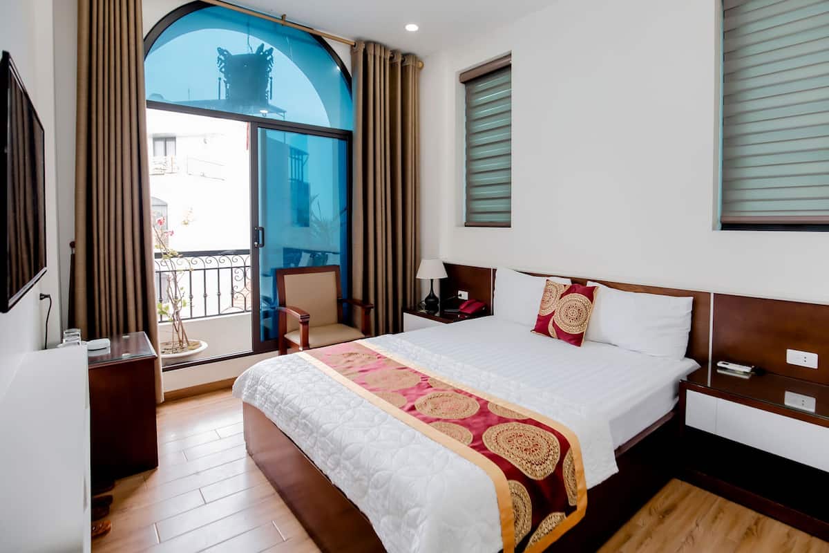 A hotel room with a large bed, a chair, a desk, and a balcony with a view.