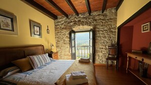 Una camera da letto con parete in pietra, soffitto in legno, un letto con cuscino a righe, un comodino, una sedia e un tavolo.
