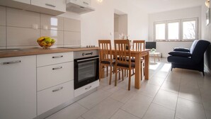 A modern kitchen with white cabinets, a built-in oven, and a dining area with wooden chairs and a table. - Cosy apartment for 4 people with A/C, WIFI, TV and terrace (Senj)