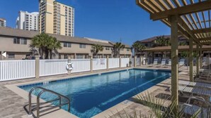 A swimming pool with a wooden pergola and lounge chairs, surrounded by a white fence and palm trees. - Sea Star, Gulf-side townhome, 2-minute walk to the beach (Navarre)