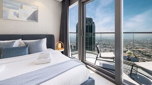 A modern hotel room with a large bed, a view of the city through floor-to-ceiling windows, and a balcony with a table and chair. - 2BR |Sea & City Views |Infinity Pool |High Floor (Dubai)