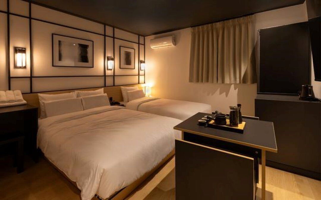 A hotel room with two beds, a desk, and a TV.