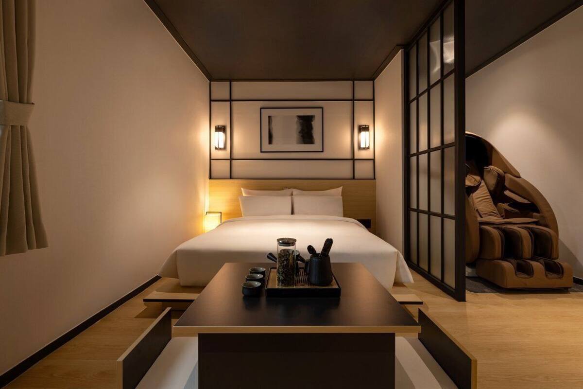 A modern hotel room with a neatly made bed, a massage chair, and a small table with tea set.