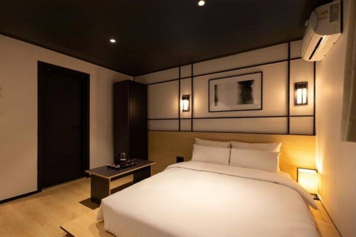 A hotel room with a large bed, bedside tables, a nightstand, a wall-mounted air conditioner, and a framed picture above the bed.