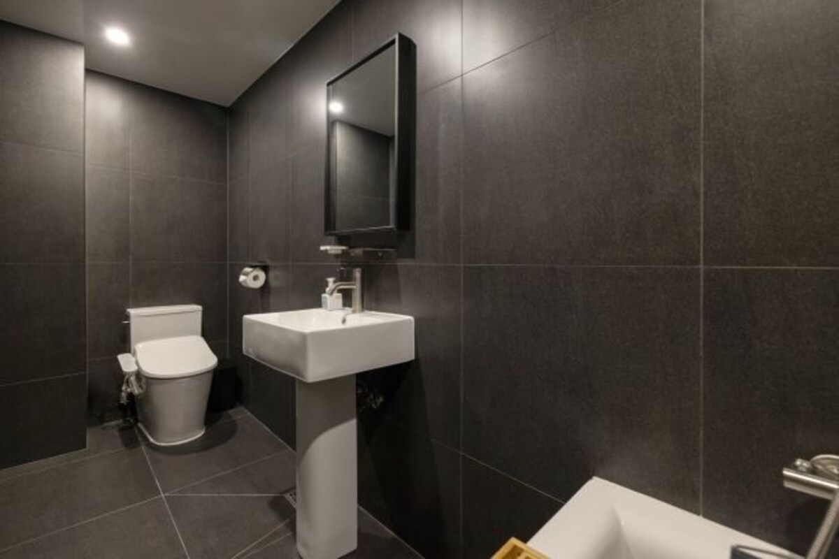 Un baño moderno con baldosas oscuras, un lavabo blanco y un inodoro.