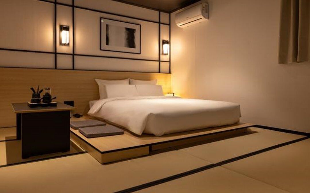 A modern hotel room with a bed, bedside table, and wall-mounted air conditioning unit.