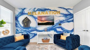 En stue med et blåt sofasæt, et hvidt sofabord og et vægmaleri med ordet "MELANATION".