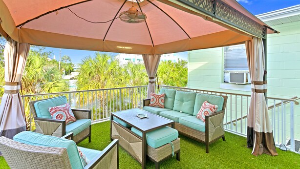 An outdoor patio with wicker furniture, a table, and an umbrella providing shade. - easy access to beach, large family retreat, huge outdoor area (Treasure Island)