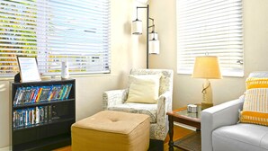 A living room with a bookshelf, a patterned armchair, a beige ottoman, a white sofa with orange cushions, and a lamp. - easy access to beach, large family retreat, huge outdoor area (Treasure Island)