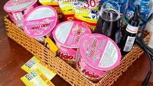 Un panier en osier rempli de divers produits alimentaires, notamment des en-cas emballés dans des emballages roses et des boissons en bouteille.