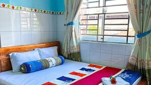 Un lit bien fait, avec une couverture colorée, une tête de lit en bois et une fenêtre avec des rideaux.