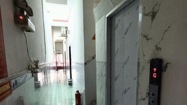 Un couloir au sol en marbre, équipé d’un extincteur, d’un panneau indiquant un espace fumeurs et d’un panneau de commande d’ascenseur fixé au mur.
