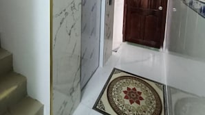 Un couloir avec un mur en marbre, une porte en bois et un sol carrelé.