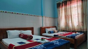 Une chambre avec deux lits en bois, chacun doté d’un matelas blanc et d’une couverture rouge et bleue.