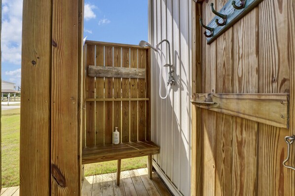 A wooden outdoor shower enclosure with a bench, a hose, and a soap dispenser.