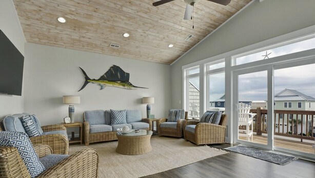 Un salon spacieux, meublé de meubles en osier, agrémenté d’un grand tableau mural représentant des poissons et offrant une vue sur la terrasse.
