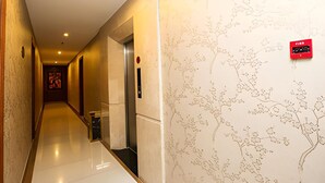 Corredor de hotel com piso polido, uma placa de saída de emergência vermelha e uma parede com padrão de árvore.