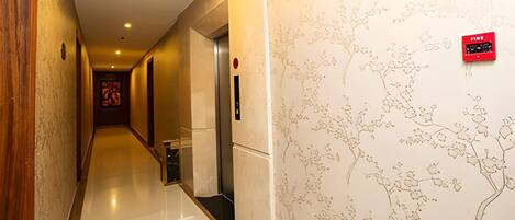A hotel hallway with a polished floor, a red emergency exit sign, and a wall with a tree-like pattern.