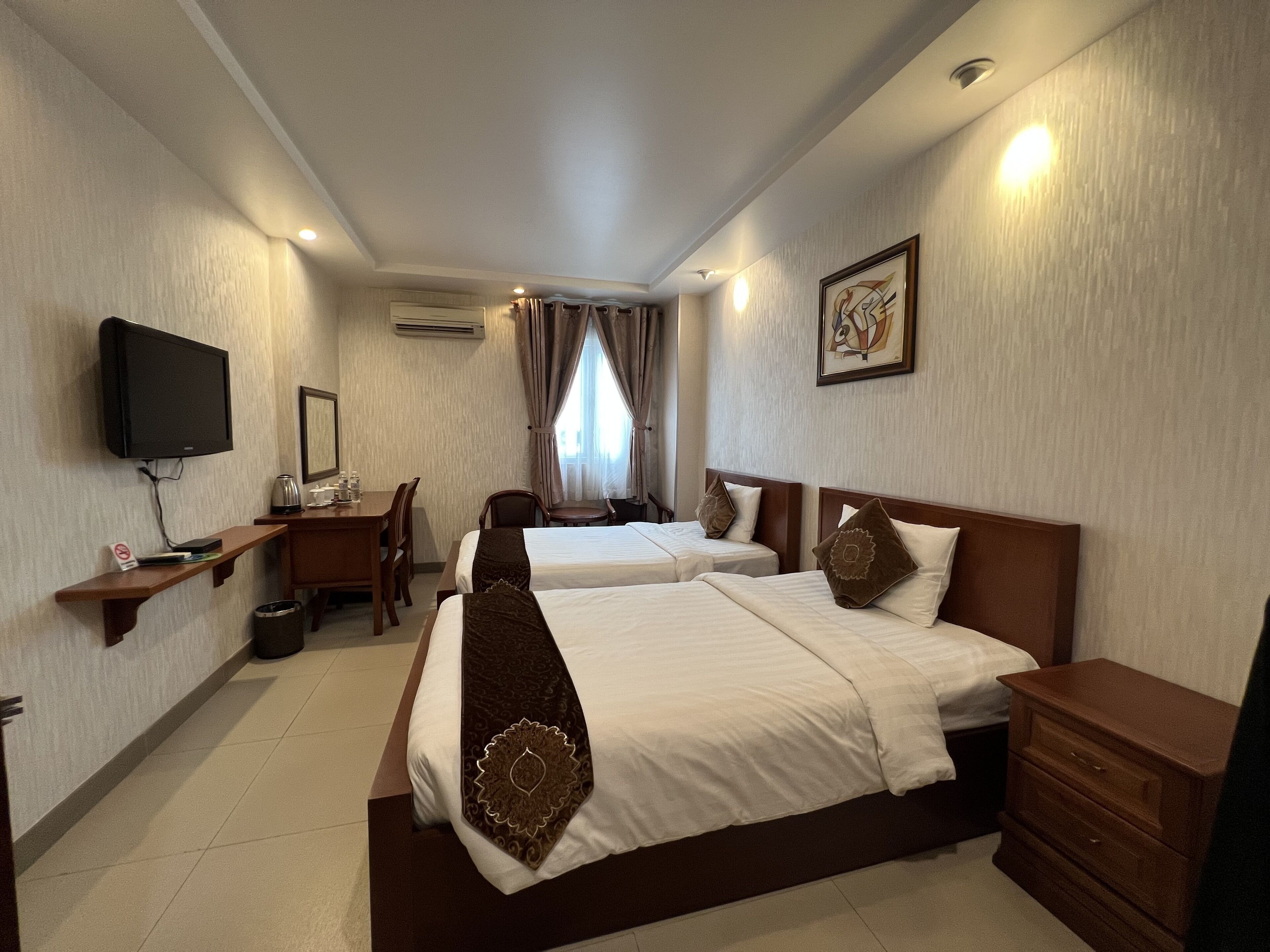 A hotel room with two beds, a desk, a chair, a TV, and a dresser.