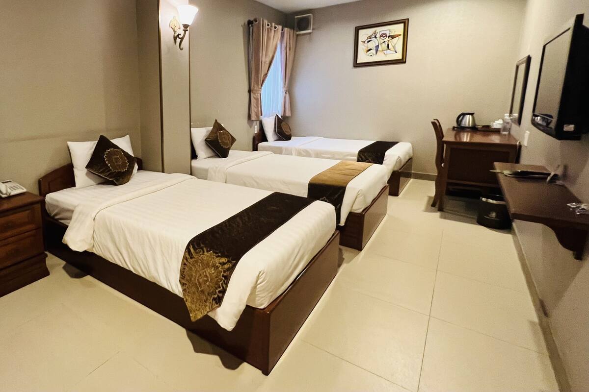 Habitación de hotel con dos camas, una mesita de noche con lámpara, un escritorio con silla y un televisor de pantalla plana en la pared.