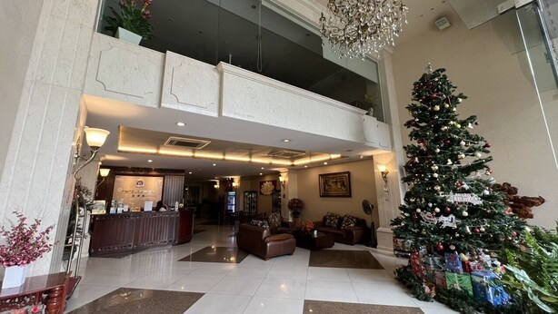 Um saguão de hotel com balcão de recepção, área de estar e uma árvore de Natal decorada.
