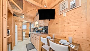 A wooden cabin interior with a dining area, kitchen, and a mounted flat-screen TV. - Lolli's Lil Getaway (Alma)