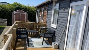 A wooden deck with outdoor seating and a small table, a shed, and a house with a sliding glass door.