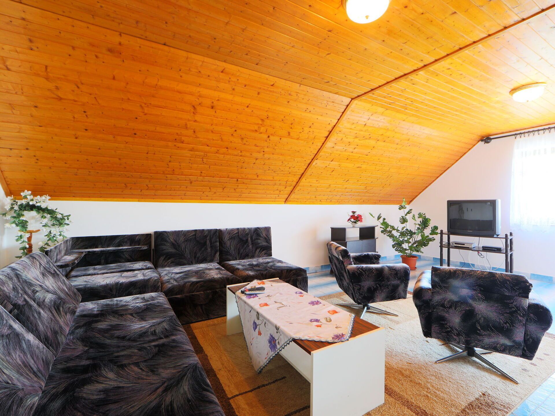 A cozy living room with a wooden ceiling, a sofa set, a coffee table, and a TV on a stand.